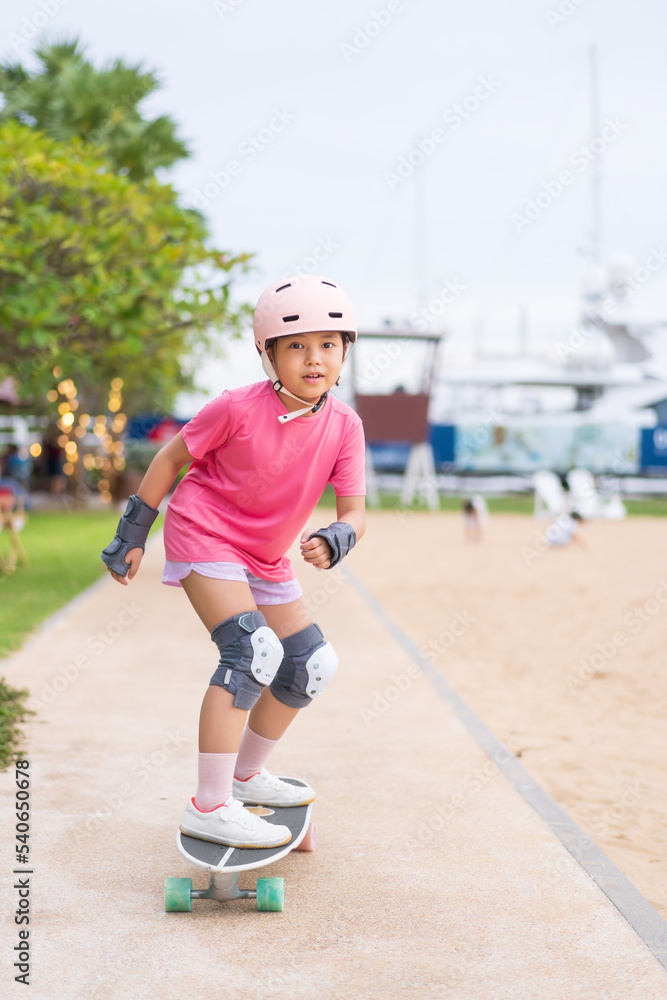 asian child or kid girl smile playing skateboard or riding surf skate carving and fun in skate park track on summer at beach for extreme sports exercise to wearing helmet wrist support for body safety