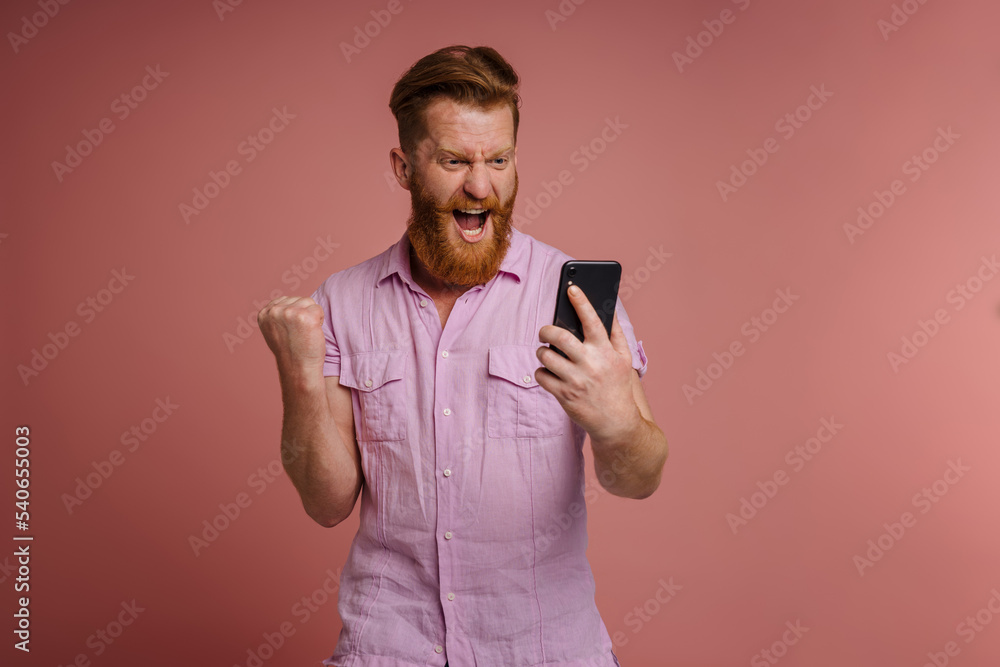 Adult stylish redhead bearded enthusiastic man holding and looking phone Adult stylish redhead bearded enthusiastic man holding and looking phone