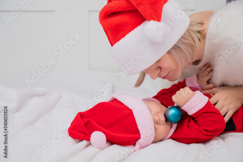 Caucasian woman hugging baby son in santa claus costume. 