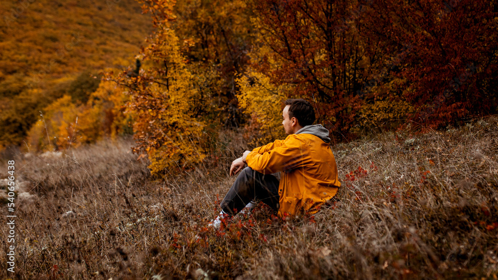 a man in a yellow jacket sits on withered grass in the autumn forest a man in a yellow jacket sits on withered grass in the autumn forest