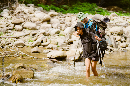 Fototapeta Naklejka Na Ścianę i Meble -  White young travelers with backpacks hiking through forest river