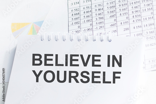 BELIEVE IN YOURSELF text on blue wooden background with charts