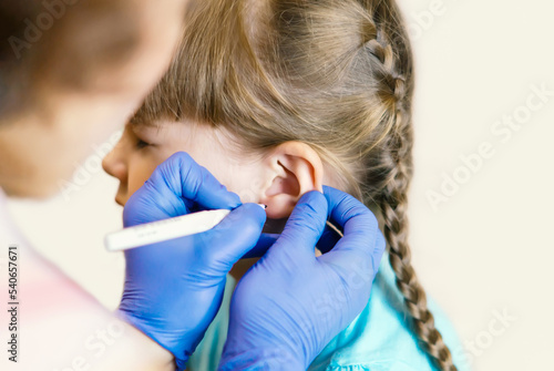 Cuadro en lienzo A charming little girl is undergoing the procedure of ear piercing by a professional medical worker