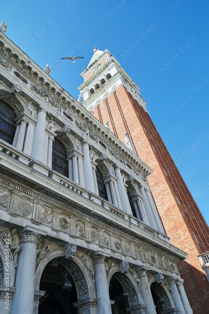 The tower St Mark's Campanile and facade with gallery of Biblioteca Marciana on the St Mark's square in Venice, Italy. With bright blue sky on the background