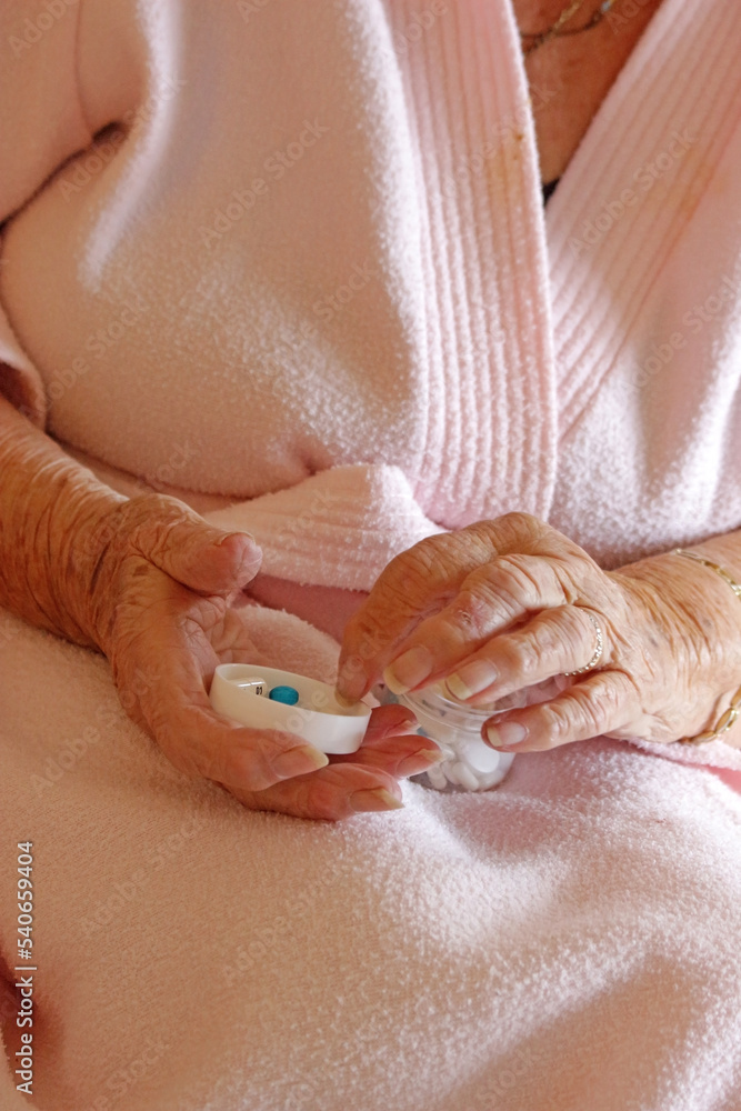 A senior woman picking up a pill out of a medicine pot which is on her lap. A senior woman picking up a pill out of a medicine pot which is on her lap.