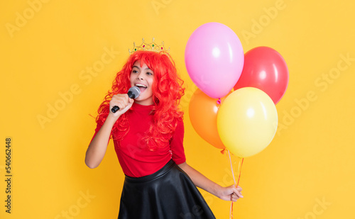glad kid in crown with microphone and party balloon on yellow background
