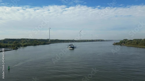 Aerial footage of cargo ship moving on wide river. Row of wind power stations along riverbank. Transport and logistics concept. Barendrecht, Netherlands photo