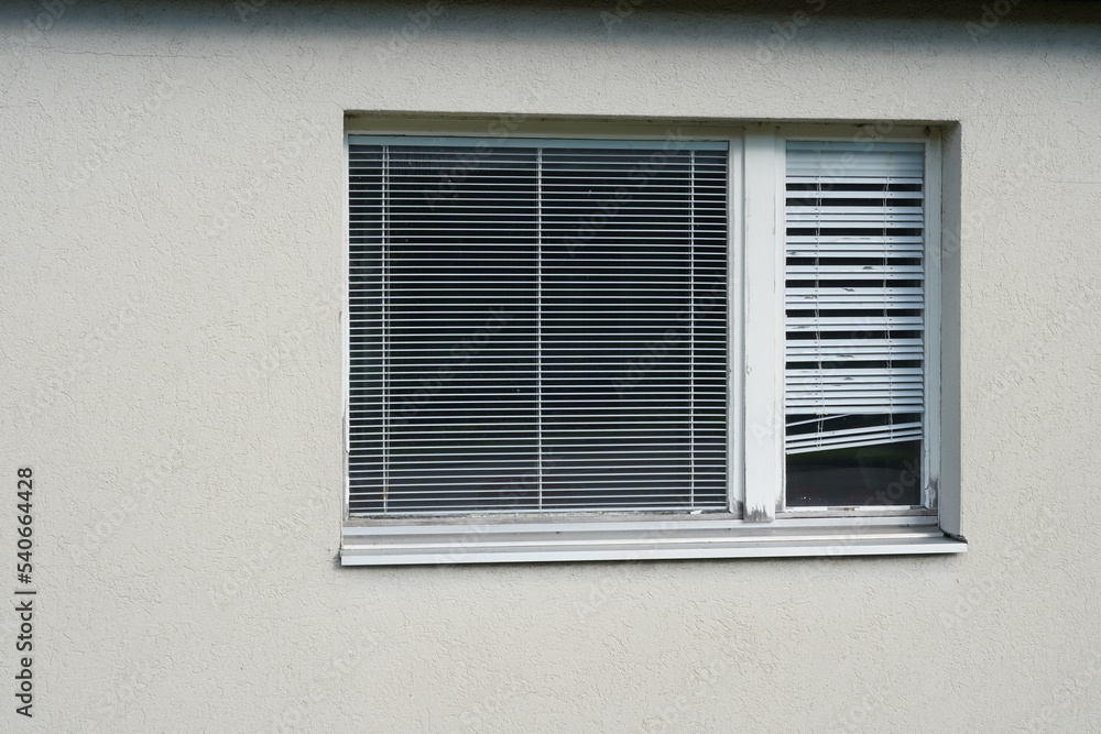 Fototapeta premium Closed window with a wooden frame with intern shutters. The color of the frame is partly peeling off and the lamellas of the shutters are distorted on several place. Cutout of a house facade.