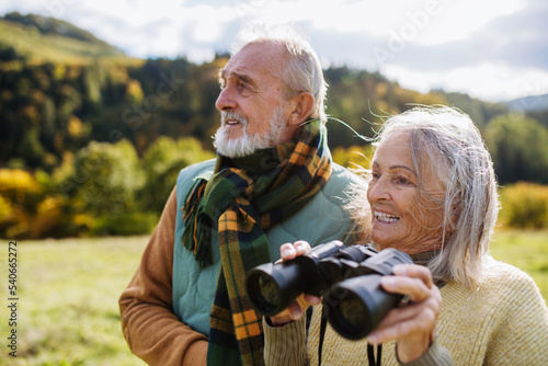 Senior couple looking at view trough binoculars on autumn walk.