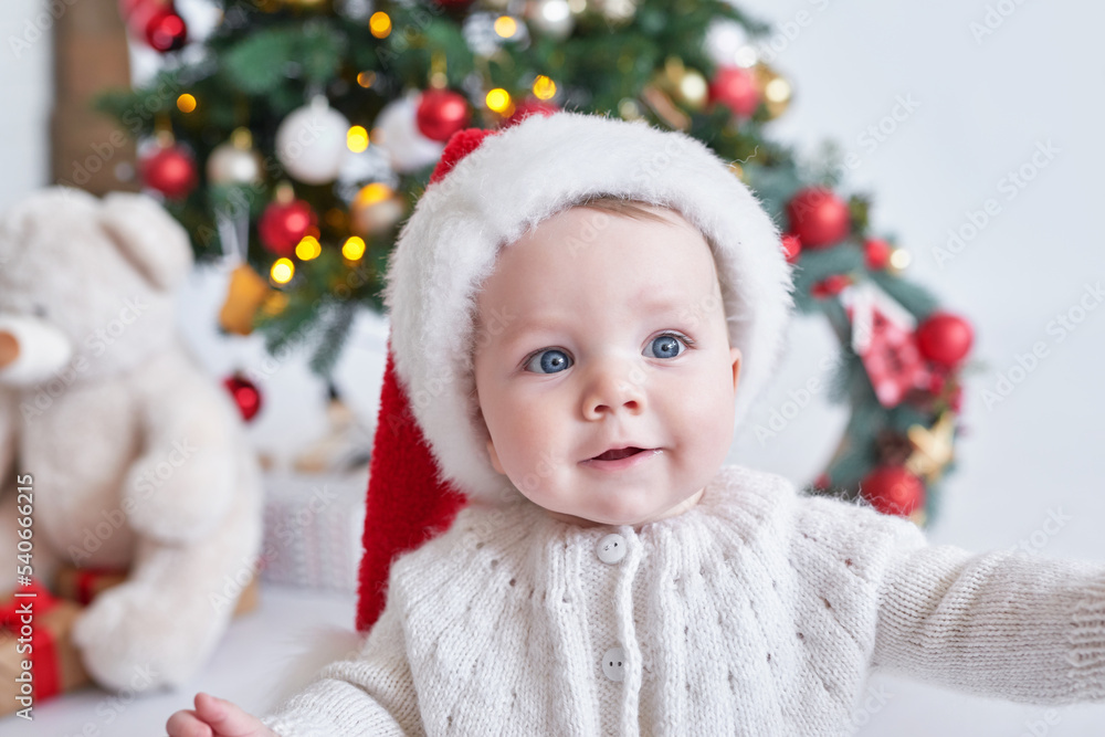 Santa baby. Christmas tree background. Happy New Year! Child in Santa's hat. Santa baby. Christmas tree background. Happy New Year! Child in Santa's hat.