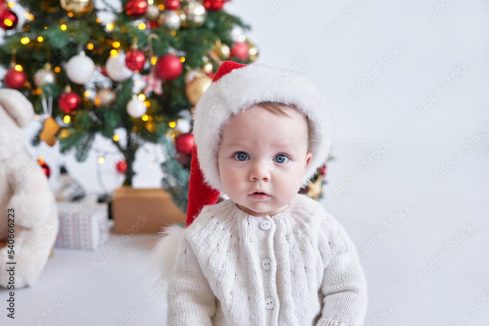 Santa baby. Christmas tree background. Happy New Year! Child in Santa's hat. Santa baby. Christmas tree background. Happy New Year! Child in Santa's hat.