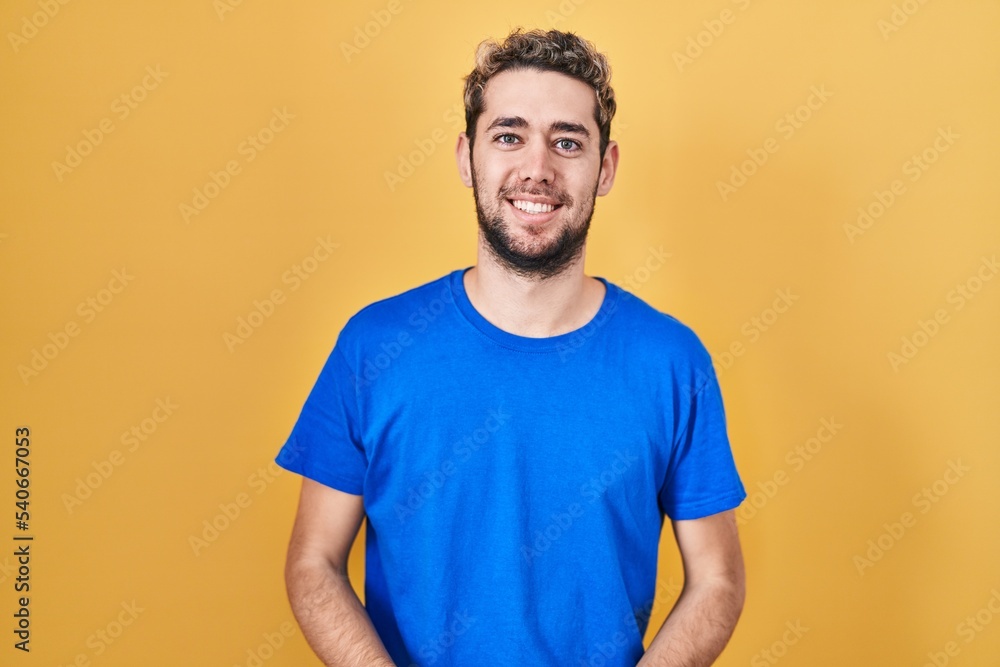 Hispanic man with beard standing over yellow background with hands together and crossed fingers smiling relaxed and cheerful. success and optimistic Hispanic man with beard standing over yellow background with hands together and crossed fingers smiling relaxed and cheerful. success and optimistic