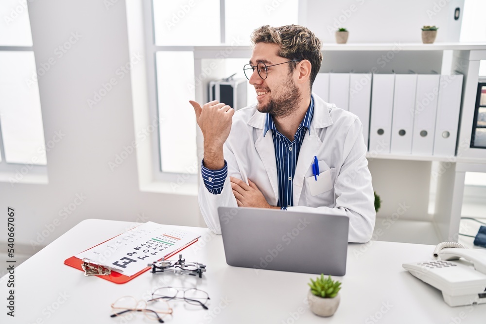 Hispanic man with beard wearing doctor uniform and stethoscope pointing thumb up to the side smiling happy with open mouth Hispanic man with beard wearing doctor uniform and stethoscope pointing thumb up to the side smiling happy with open mouth