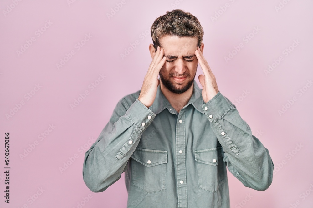 Hispanic man with beard standing over pink background with hand on head for pain in head because stress. suffering migraine. Hispanic man with beard standing over pink background with hand on head for pain in head because stress. suffering migraine.
