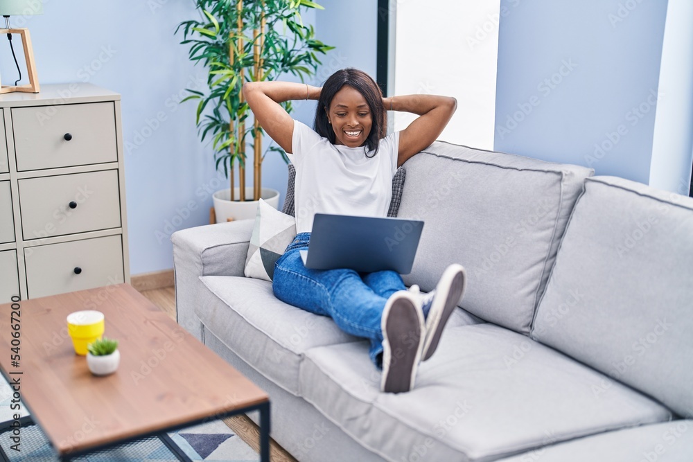 Young african american woman using laptop sitting on sofa at home Young african american woman using laptop sitting on sofa at home