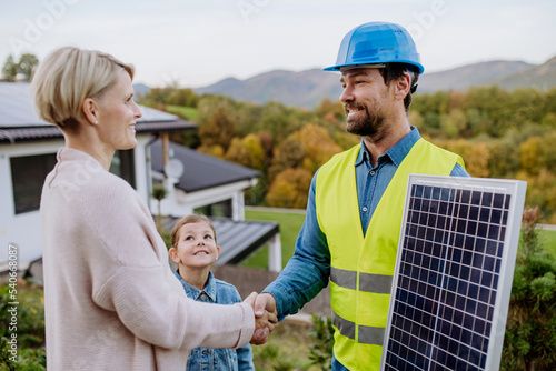 Smiling handyman, photovoltaics panels installer shaking hand with family owner of house. © Halfpoint