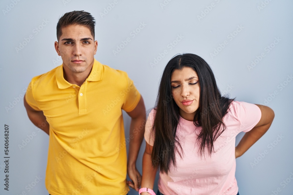 Young couple standing over isolated background suffering of backache, touching back with hand, muscular pain Young couple standing over isolated background suffering of backache, touching back with hand, muscular pain