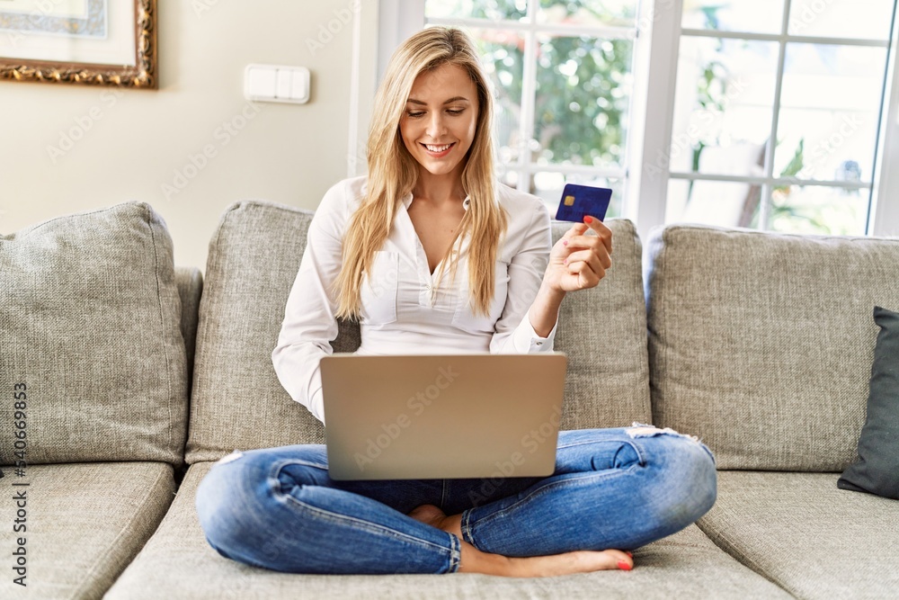 Young blonde woman buying using laptop and credit card sitting on the sofa at home. Young blonde woman buying using laptop and credit card sitting on the sofa at home.