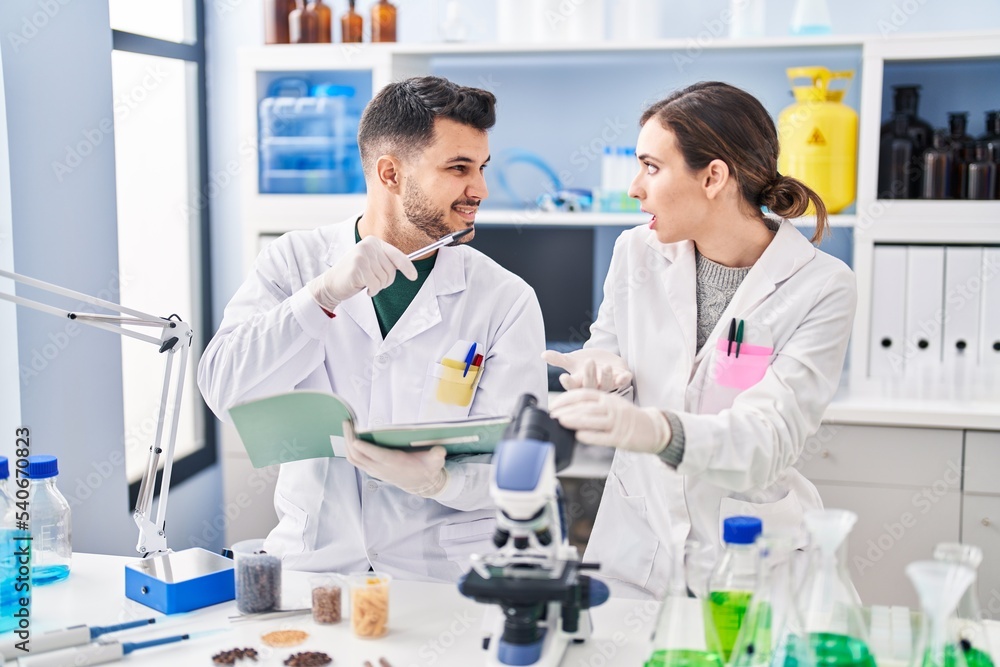 Man and woman wearing scientist uniform writing on notebook at laboratory Man and woman wearing scientist uniform writing on notebook at laboratory