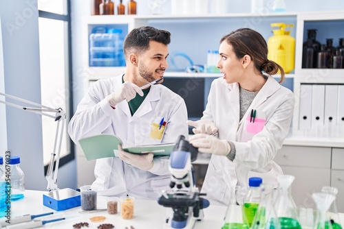 Man and woman wearing scientist uniform writing on notebook at laboratory