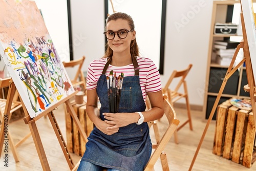 Cuadro en lienzo Young woman smiling confident holding paintbrushes at art studio