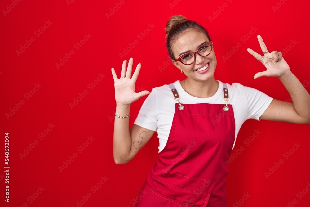 Young hispanic woman wearing waitress apron over red background showing and pointing up with fingers number eight while smiling confident and happy. Young hispanic woman wearing waitress apron over red background showing and pointing up with fingers number eight while smiling confident and happy.