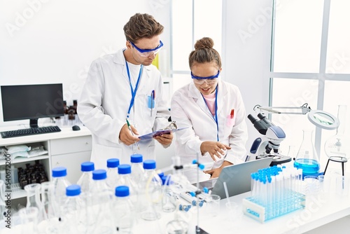 Man and woman wearing scientist uniform using laptop working at laboratory