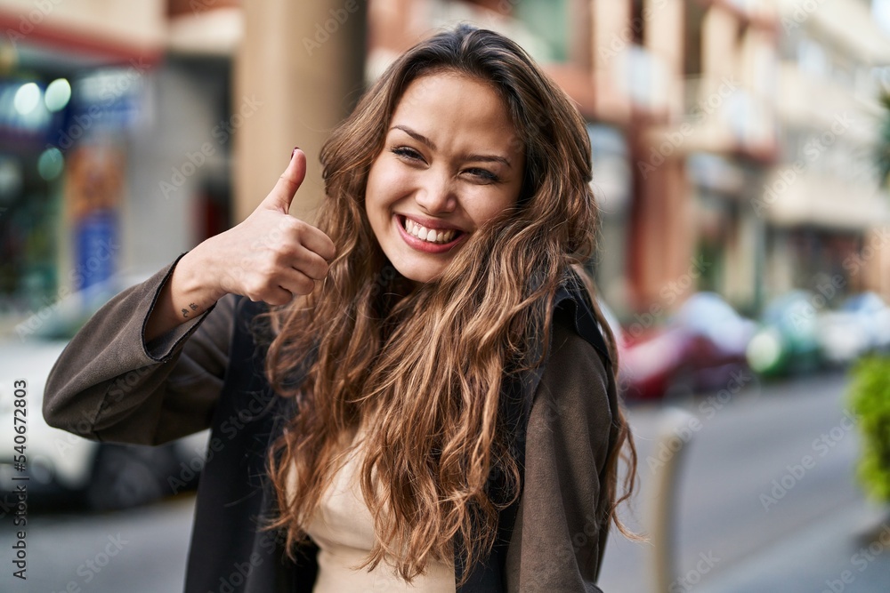 Young beautiful hispanic woman smiling confident doing ok sign with thumb up at street
