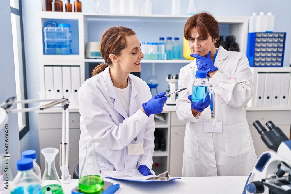 Two women scientists holding test tube writing on document at laboratory Two women scientists holding test tube writing on document at laboratory