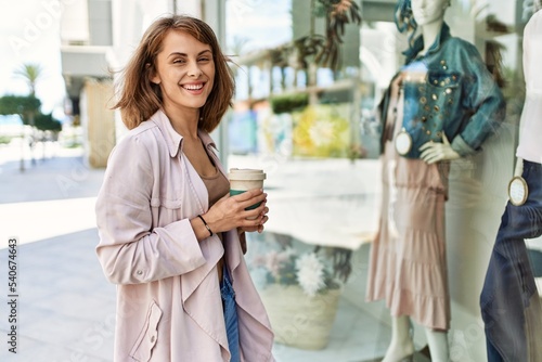 Young caucasian girl drinking coffee and looking showcase of clothing store at the city.