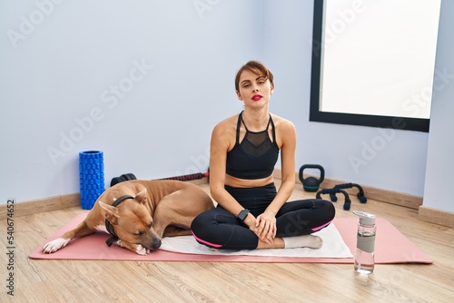 Young beautiful woman sitting on yoga mat relaxed with serious expression on face. simple and natural looking at the camera.