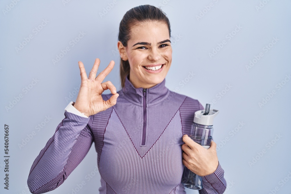 Beautiful woman wearing sportswear holding water bottle smiling positive doing ok sign with hand and fingers. successful expression. Beautiful woman wearing sportswear holding water bottle smiling positive doing ok sign with hand and fingers. successful expression.