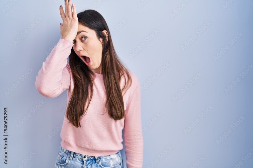 Young brunette woman standing over blue background surprised with hand on head for mistake, remember error. forgot, bad memory concept. Young brunette woman standing over blue background surprised with hand on head for mistake, remember error. forgot, bad memory concept.