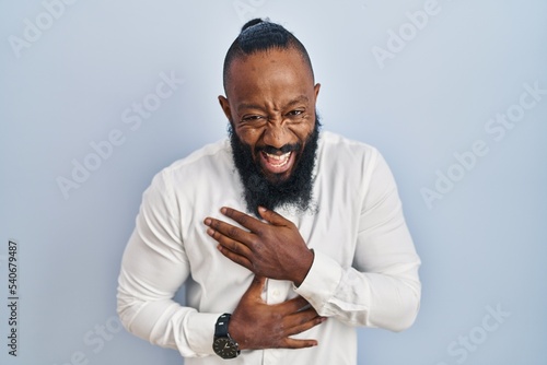 African american man standing over blue background smiling and laughing hard out loud because funny crazy joke with hands on body.