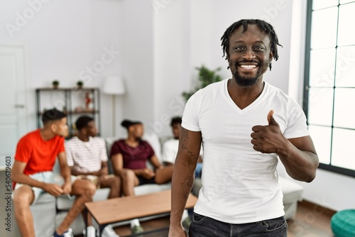 Young african man with friends at the living room smiling happy and positive  thumb up doing excellent and approval sign