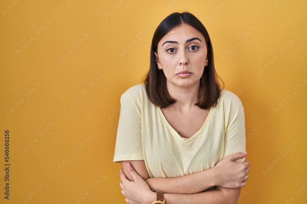 Hispanic girl wearing casual t shirt over yellow background shaking and freezing for winter cold with sad and shock expression on face Hispanic girl wearing casual t shirt over yellow background shaking and freezing for winter cold with sad and shock expression on face
