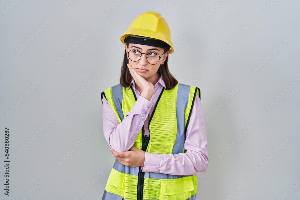 Hispanic girl wearing builder uniform and hardhat thinking looking tired and bored with depression problems with crossed arms. Hispanic girl wearing builder uniform and hardhat thinking looking tired and bored with depression problems with crossed arms.