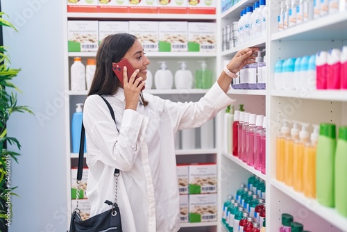Young beautiful hispanic woman customer smiling confident talking on smartphone at pharmacy
