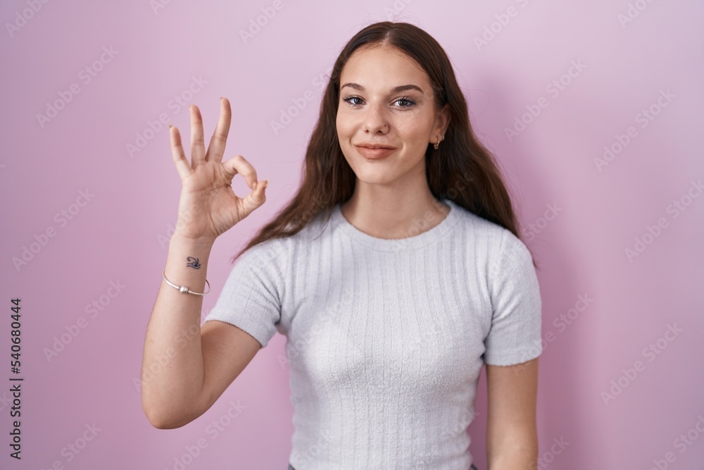 Young hispanic girl standing over pink background smiling positive doing ok sign with hand and fingers. successful expression. Young hispanic girl standing over pink background smiling positive doing ok sign with hand and fingers. successful expression.