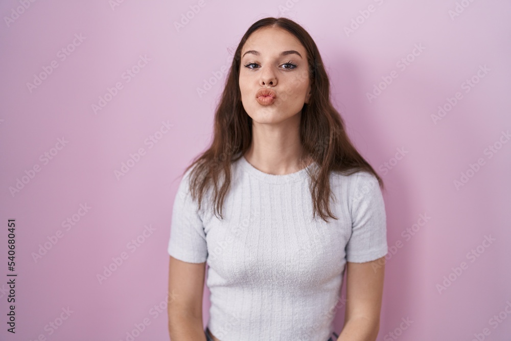 Young hispanic girl standing over pink background looking at the camera blowing a kiss on air being lovely and sexy. love expression. Young hispanic girl standing over pink background looking at the camera blowing a kiss on air being lovely and sexy. love expression.
