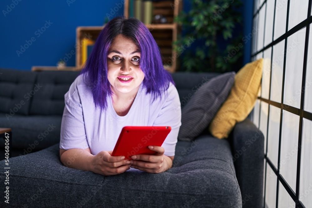 Young beautiful plus size woman using touchpad lying on sofa at home Young beautiful plus size woman using touchpad lying on sofa at home