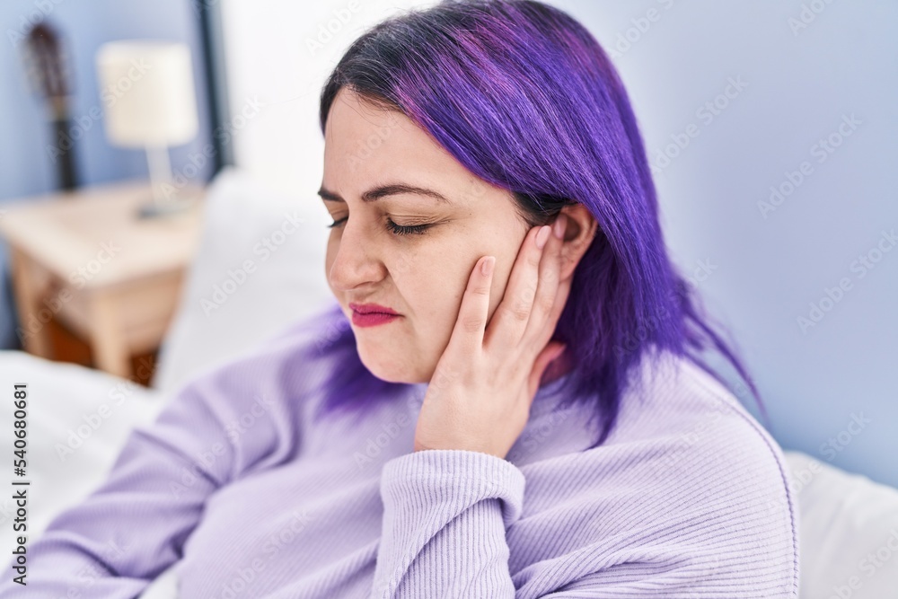 Young beautiful plus size woman suffering for ear pain sitting on bed at bedroom Young beautiful plus size woman suffering for ear pain sitting on bed at bedroom