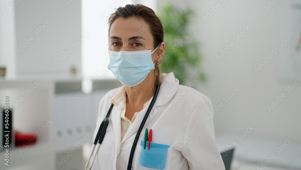 Middle age hispanic woman wearing doctor uniform and medical mask at clinic Middle age hispanic woman wearing doctor uniform and medical mask at clinic