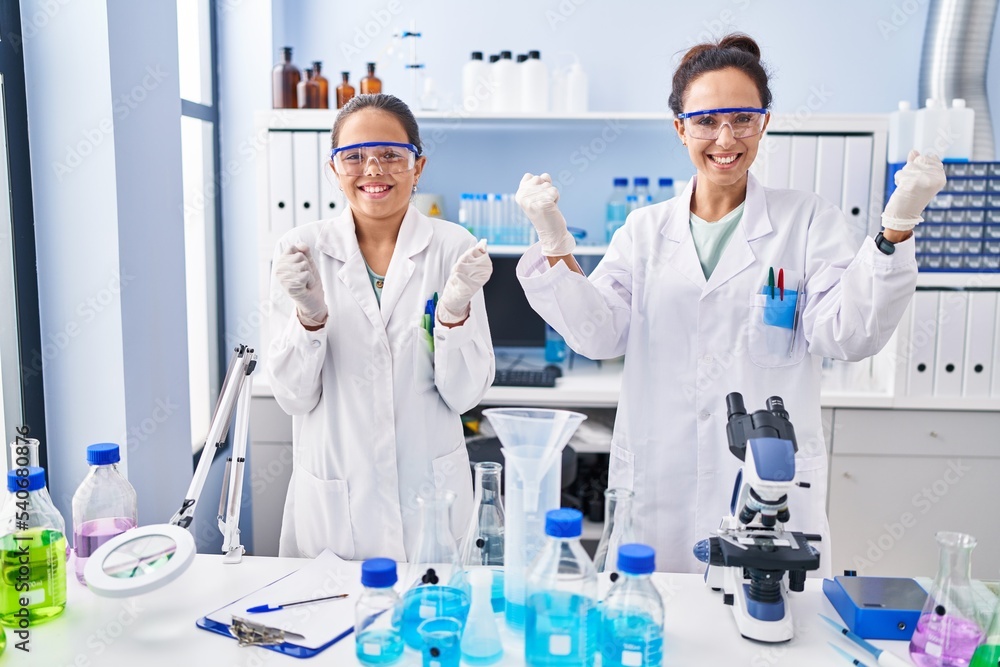 Young mother and daughter at scientist laboratory screaming proud, celebrating victory and success very excited with raised arms Young mother and daughter at scientist laboratory screaming proud, celebrating victory and success very excited with raised arms