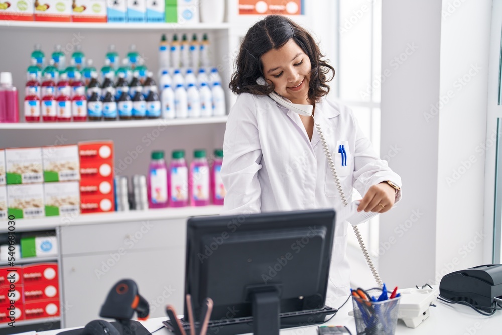 Young woman pharmacist talking on telephone reading prescription at pharmacy Young woman pharmacist talking on telephone reading prescription at pharmacy
