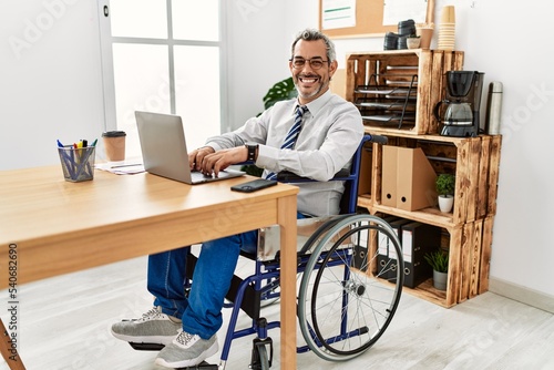 Middle age hispanic man working at the office sitting on wheelchair with a happy and cool smile on face. lucky person.