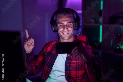 Young caucasian man playing video games with smartphone smiling happy pointing with hand and finger to the side