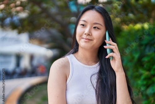Young chinese woman smiling confident talking on the smartphone at park