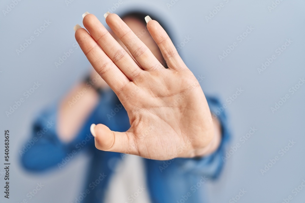 Obraz premium Hispanic woman standing over blue background covering eyes with hands and doing stop gesture with sad and fear expression. embarrassed and negative concept.