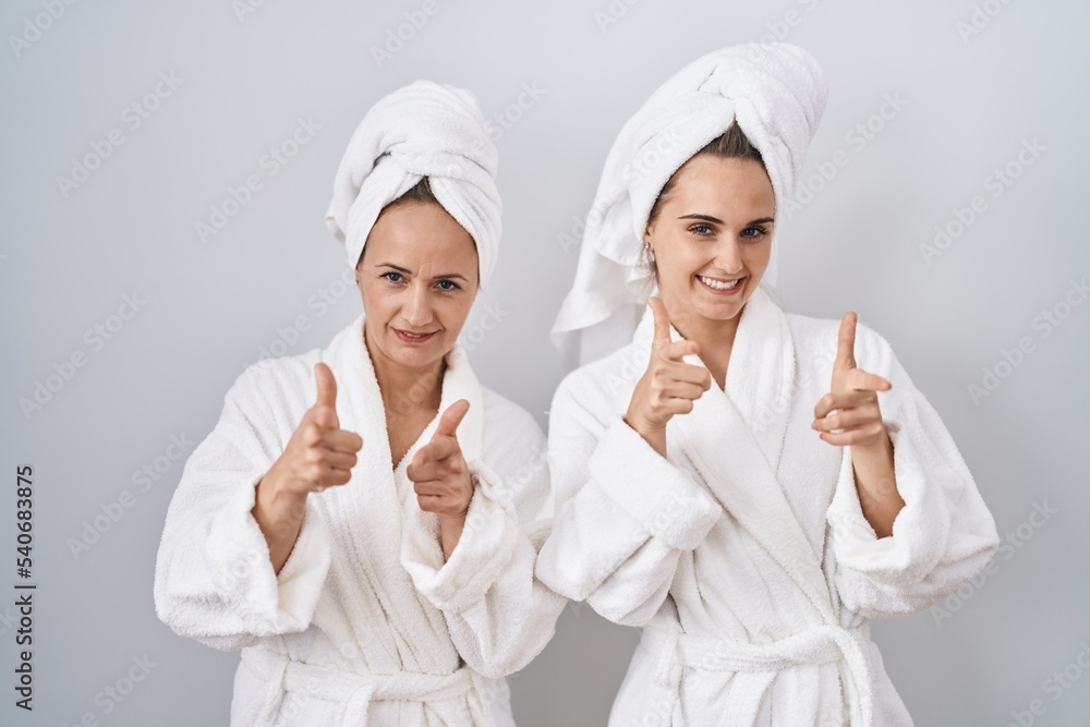 Middle age woman and daughter wearing white bathrobe and towel pointing fingers to camera with happy and funny face. good energy and vibes. Middle age woman and daughter wearing white bathrobe and towel pointing fingers to camera with happy and funny face. good energy and vibes.